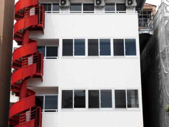 赤い外階段のある建物外観 外観   白い外壁に赤い外階段が映える、すっきりした建物です。採光のよさそうな窓が並び、館内での働きやすさを感じられます。