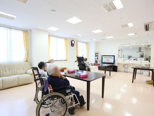 共有スペースでの日常 共有スペース 広々としたダイニングルームで、車椅子の方がリラックスしながら過ごされています。ソファやテレビがある明るく快適な空間です。
