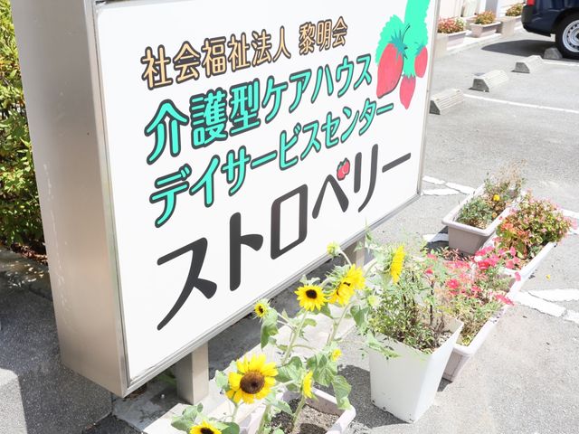 看板と花の様子 表示板 入口を彩る鮮やかな花々が訪れる方々を温かく迎えてくれます。明るい印象を与える看板です。