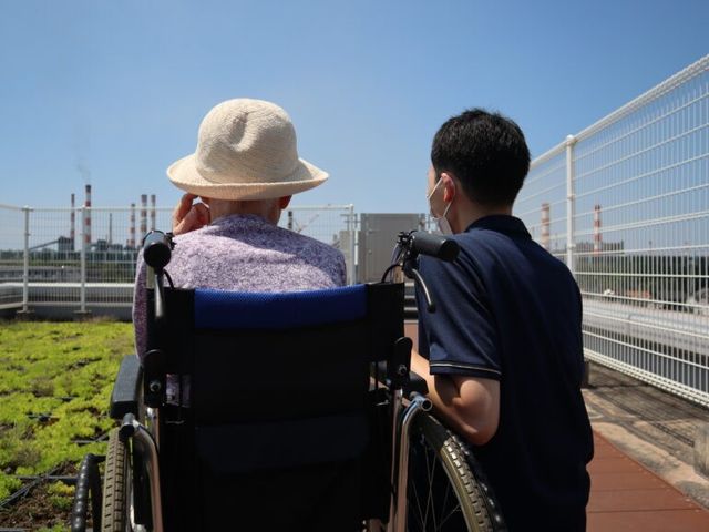 青空の下での会話 テラス 開放感のあるテラスで、心地よい風を感じながらくつろげます。職員が入居者を支援しています。