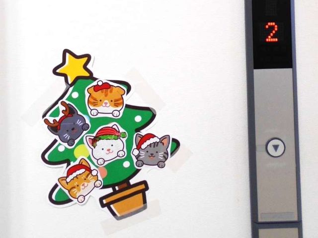 装飾されたエレベーター横 エレベーター   クリスマス風の飾りが貼られた明るい壁面です。ボタン表示も見え、分かりやすい移動設備になっています。