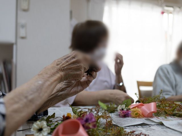 高齢者が活動中の部屋 多目的室 大きな窓から自然光が降り注ぎ、リラックスできる落ち着いた空間です。高齢者がゆったりと活動に参加しています。