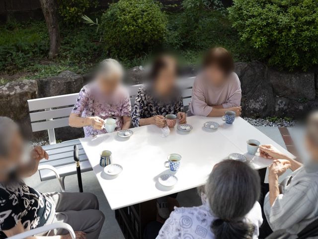 庭での憩いの様子 庭 自然に囲まれた庭で、入居者の方々が穏やかに談笑しながらお茶を楽しんでいます。