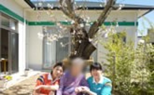 桜の木と職員の様子 中庭 桜の木の下でリラックスすることができ、職員が利用者との交流を大切にしています。