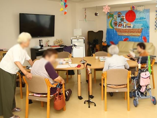 共有スペース ラウンジ 明るいスペースで、入居者の方々がゆったりと過ごしています。室内にはカラフルな飾りがあり、和やかな雰囲気が漂っています。