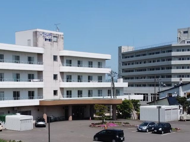 建物外観の正面 外観   青空の下に、複数階建ての建物がゆったりと並んでいます。車寄せや駐車スペースも見え、落ち着いた雰囲気です。