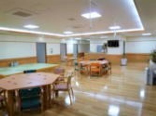 施設の写真 広い共有スペースには木製の大きなダイニングテーブルが複数置かれ、家具と家具の間には十分スペースがある。