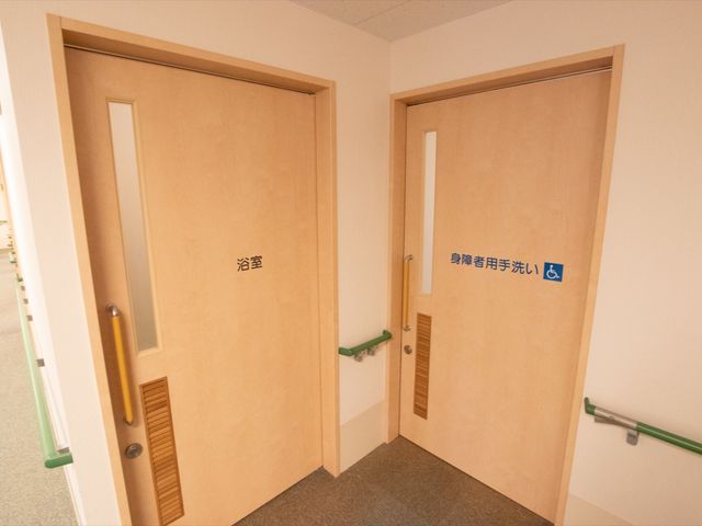 廊下の扉と案内表示 通路 手すり完備の廊下には、分かりやすい案内板が設置されており、安心してご移動いただけます。公私の時間がしっかりと分けられる、充実した設備の中で働ける環境です。