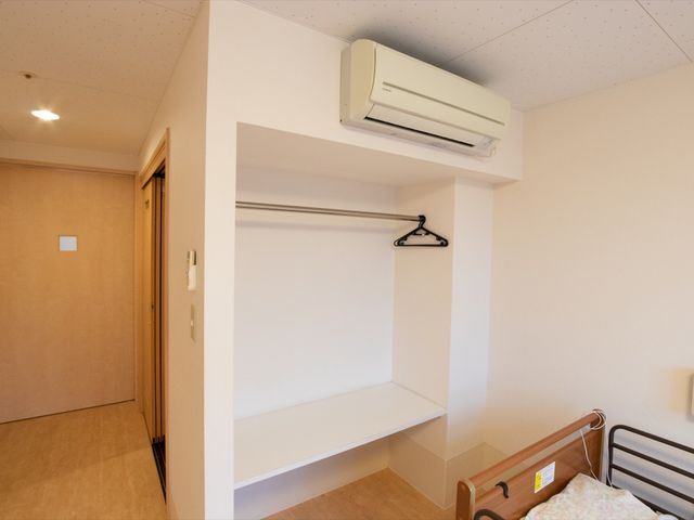清潔な居室の一角 居室 快適で暖かい環境を提供する居室です。手すり付きのベッドと広々としたクローゼットスペースが配されています。