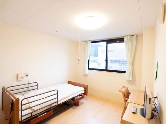 居室のベッドとデスク 居室 ゆったりとした個室は、窓の外の景色も明るく、快適なプライベート空間を提供しています。デスクとベッドが完備され、日々の生活に必要な機能を備えています。