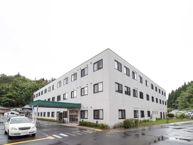 白い建物のエントランス 外観 自然に囲まれた建物の入口は、明るくて開放的です。職員としても気持ちの良い出勤ができる環境が整っています。