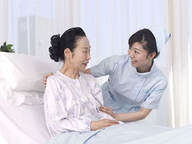 介護士と高齢女性の居室 スタッフの介助 ふとんを整える介護士と寝室で笑顔のやり取りをする優しい雰囲気のシーンです。温もりを感じるケアが行える環境が整っています。