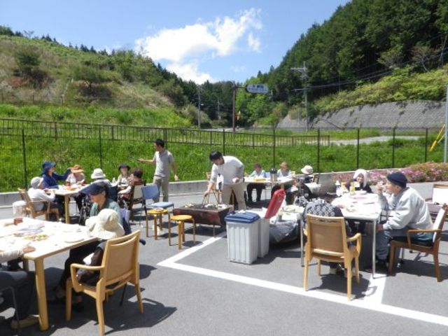 外食イベントの様子 レクリエーション 晴れた日の快適な中庭で開催される食事イベント。スタッフと利用者が交流しながら、楽しい一時を過ごしています。