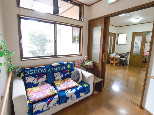 共有リビングの一角 談話スペース 暖かみのあるリビングには、ソファやテーブルが配され、窓から自然光が差し込みます。また、車椅子をご利用の方がいらっしゃる様子も伺え、利用者の方々がふれあいやくつろぎの時間を過ごせる空間となっております。