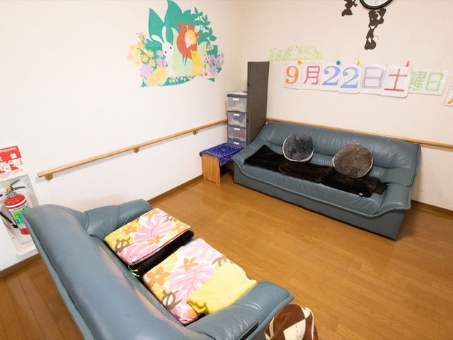 壁装飾のある居室空間 共有スペース 広々とした居室は、かわいらしい壁の装飾が印象的です。ソファにはクッションがあり、居心地の良い安らぎの場所を演出しています。