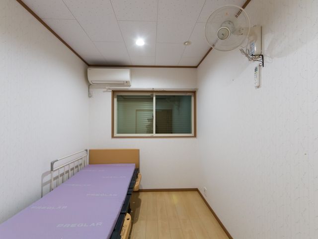 清潔感のある居室 居室 シンプルで整った部屋は、快適な日々を過ごすための配慮が行き届いています。壁に取り付けられた扇風機やエアコンも設備され、季節を問わず適温を保てます。
