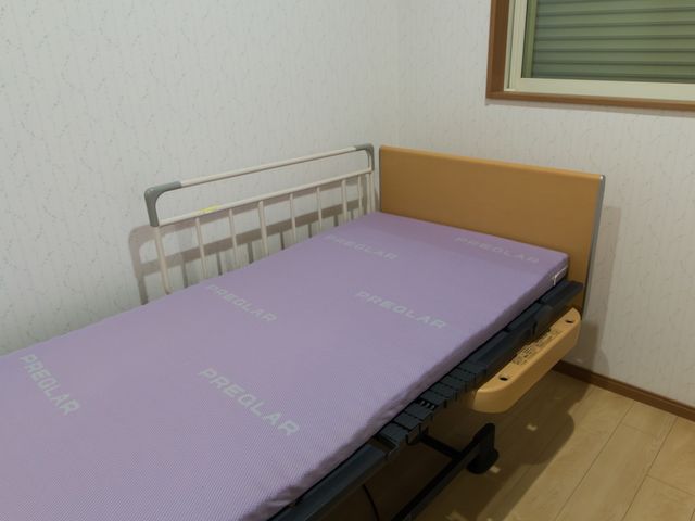 快適な居室のベッド 居室 広々とした居室の一角に、清潔感溢れるベッドが整っています。ゆとりをもっておくつろぎいただける空間です。