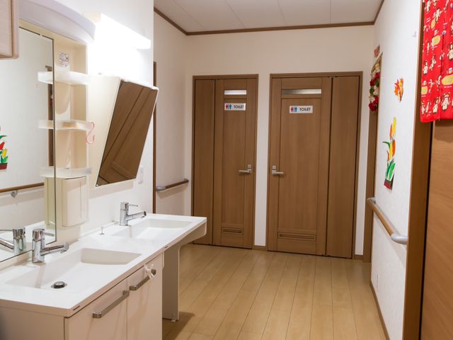 明るい洗面所とトイレ扉 洗面所 洗面台が広く、壁には手すりも設置されており、バリアフリーに配慮した清潔感のある空間です。