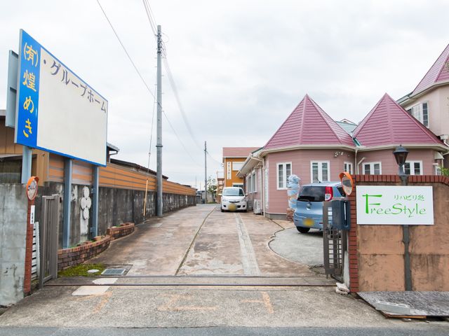 施設入口と駐車場 外観 植栽に囲まれたエントランスは、来訪者を温かく迎え入れます。ゆとりの駐車スペースも完備しておりますので、安心です。