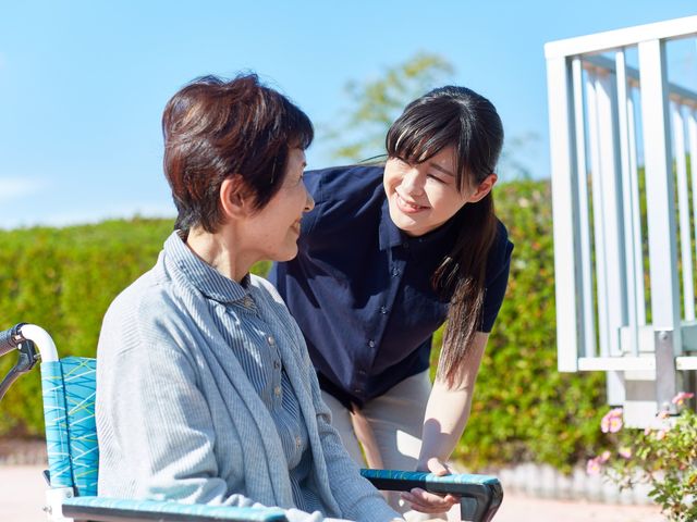 優しい会話の場面 庭 青空の下、スタッフが利用者と和やかに語らう場面が印象的です。