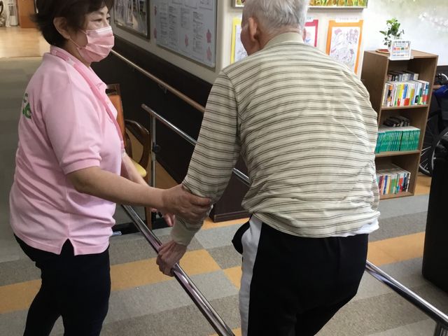 安全な歩行訓練の様子 廊下 スタッフが利用者に寄り添いながら、安心して歩行訓練が行える環境です。壁面には温かみのある飾りが施されています。