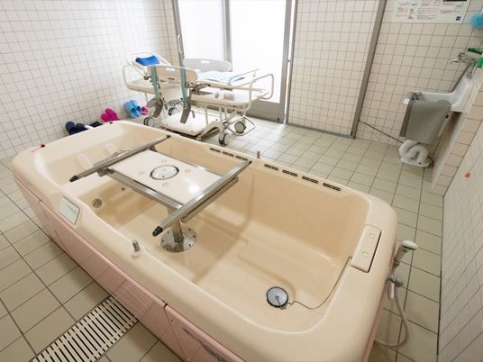 浴室内の壁や床は白系のタイル張りであり、清潔感がある。中央に大きな介護用浴槽が設置されている。入居者様は寝た状態で入浴が可能である。