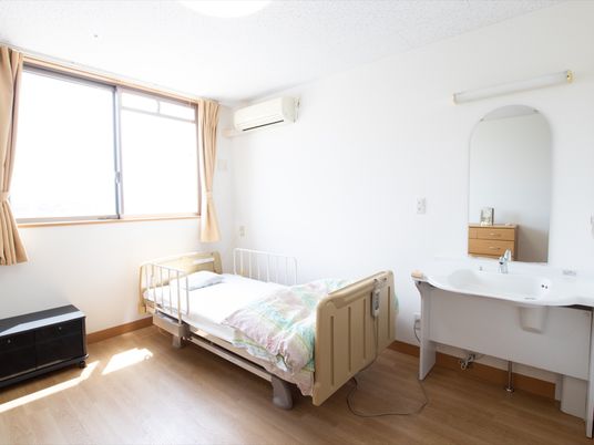 居室には、介護用の電動ベッドや車椅子対応の洗面台が設置されている。腰高の窓があり、日差しが差し込む。