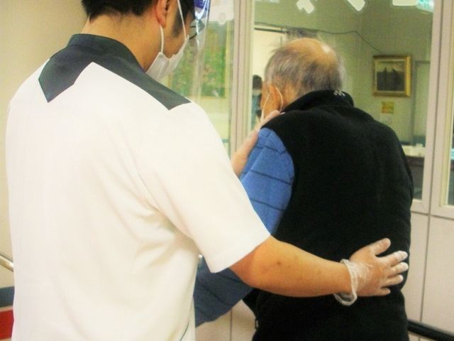 介護士が介助する場面 廊下 スタッフが丁寧に付き添い、安心して移動できるようにサポートしています。優しさが感じられます。