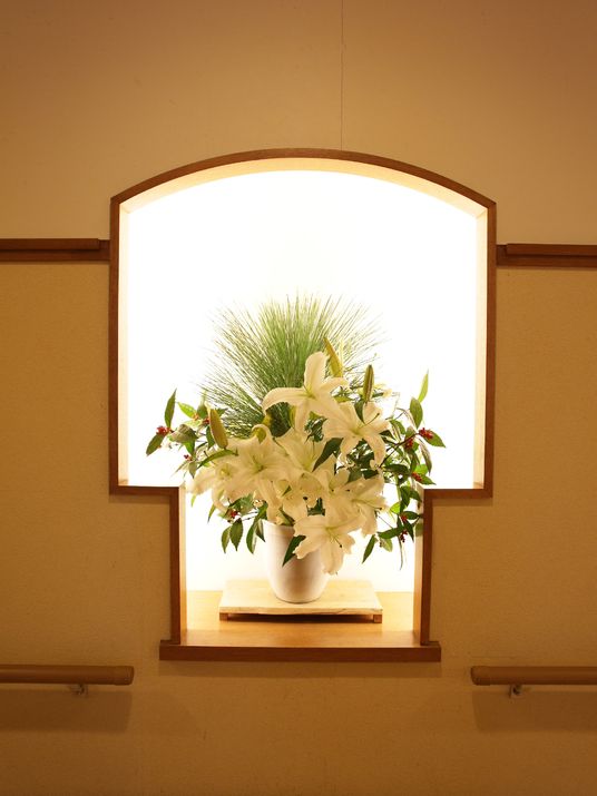 壁には床の間があり、中は照明で照らされている。木の台の上には、白い花瓶の中に白いユリの花が生けられている。