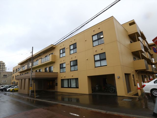 黄色い外壁の建物外観 外観 安心感を与える落ち着いた色合いの建物です。雨の日もすぐに入れる広い屋根付きのエントランスが特徴です。