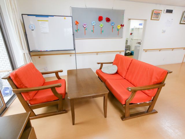 赤い布張りの椅子がある休憩室 廊下 落ち着いた色合いのリラックススペースで、休息を取りながらゆったりとした時を過ごせます。壁掛けの装飾が温かみのある雰囲気を演出しています。