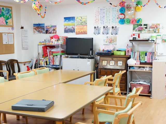 カラフルな多目的室 居間 和やかな雰囲気の多目的室です。壁には季節感を感じさせる飾りやカレンダーがあり、コミュニケーションの場として利用されています。