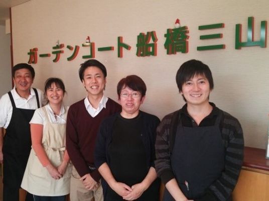 笑顔のスタッフ５人並ぶ壁前