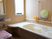 サムネイル 窓から太陽光が差し込む、白とベージュを基調にした明るい浴室。洗い場と浴槽まわりに手すりを設置、シャワーチェアも置かれている。