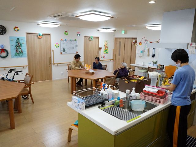 居心地の良いダイニングルーム 食堂 ゆったりとした時間が流れるダイニングスペースで、利用者同士が楽しげな会話を交わしながら過ごしています。スタッフが丁寧に調理準備をしており、安心の生活環境が整っています。