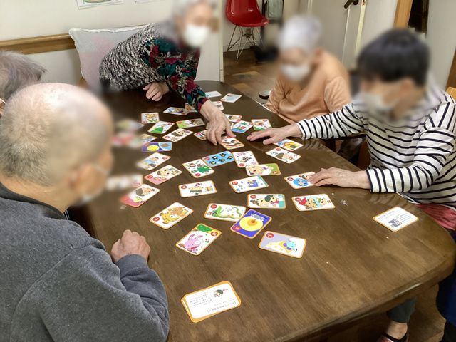 カードゲームを楽しむ卓 ラウンジ 住人がテーブルを囲み、カードゲームを楽しんでいます。温かな交流の場です。