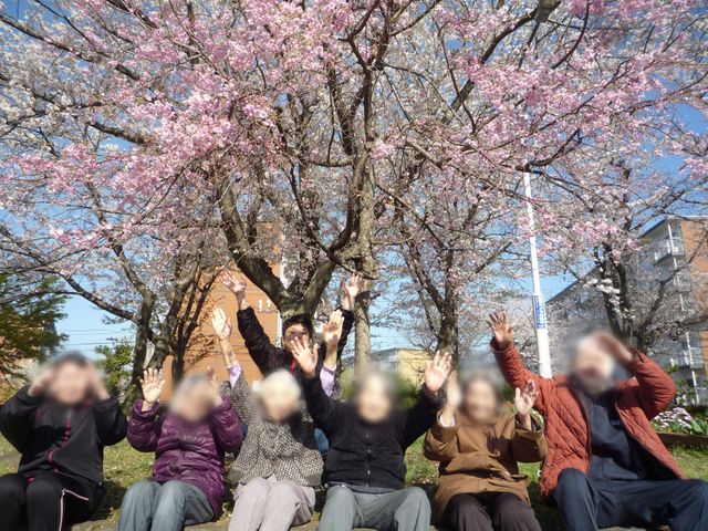笑顔の交流を楽しむ庭園 庭 満開の桜の木の下で、利用者の方々が楽しそうに交流しています。自然を感じることができる場所です。