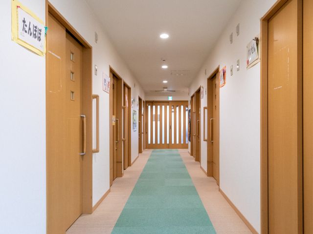 明るく広々とした廊下 廊下 温かみのある木のドアが並ぶ、柔らかい照明の廊下です。施設内の各部屋へのアクセスがスムーズです。