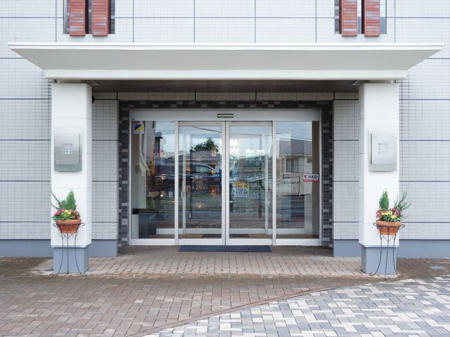 清潔な外観のエントランス 玄関 お出迎えするエントランスは、明るく清潔感があり、訪れる人を温かく迎え入れます。安心してご勤務いただける環境が整っています。