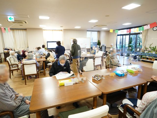 共有スペースの日常風景 共有スペース 広々とした食堂では、利用者が集い様々な活動を楽しんでいます。手作業で何かを作る姿や、大画面のテレビを視聴する姿が見られます。