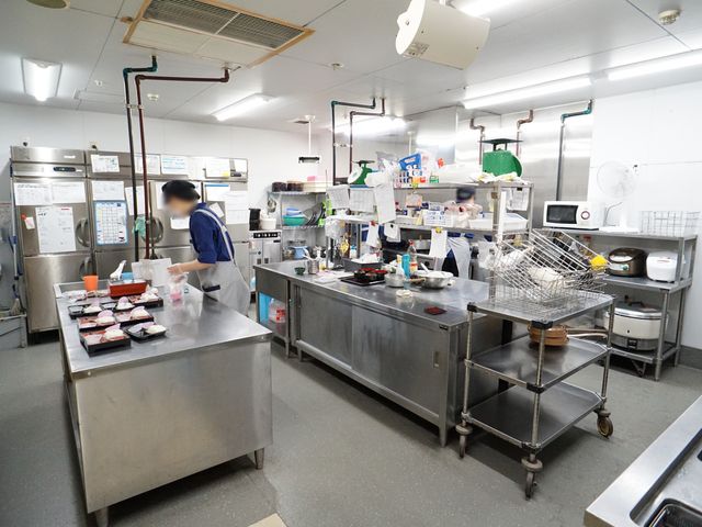 施設のキッチン作業風景 キッチン ゆとりを持った作業スペースで、スタッフが調理を行っている様子が見て取れます。清潔感あふれる環境で栄養バランスを考えた食事が提供されています。