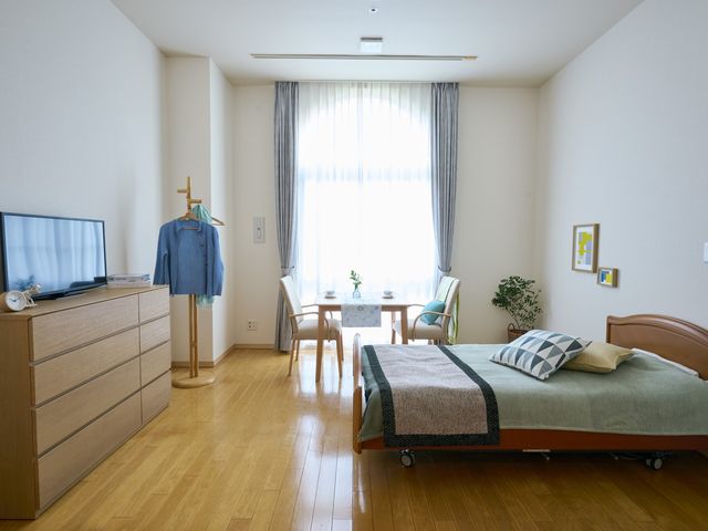 居室の明るい空間 居室 採光豊かな部屋には、安心してご利用いただけるベッドと食事スペースが備わっております。清潔感のある木目調の床が心地よい雰囲気を演出しています。