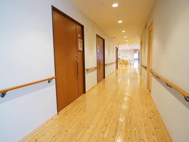 明るい木目調の廊下 廊下 手すりが備えられた廊下は、広々としており移動がしやすい設計になっています。安心して就業できる環境です。