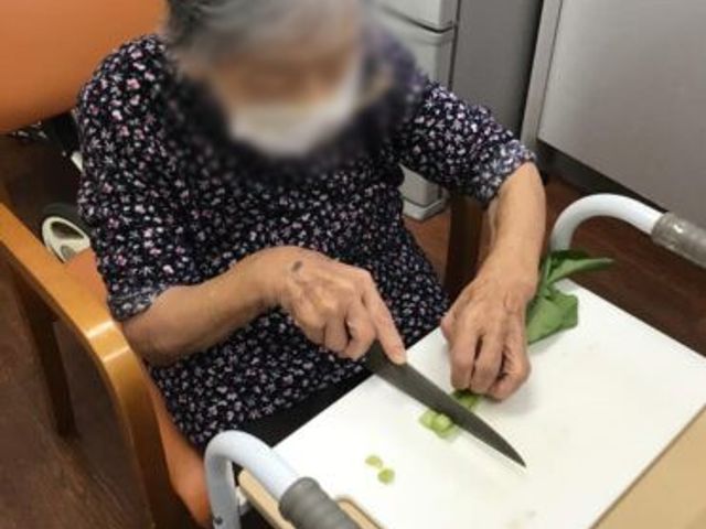 調理をする方の室内 ダイニングルーム 座って野菜を切る方の様子が見られます。調理環境が整っており、安心して利用できます。