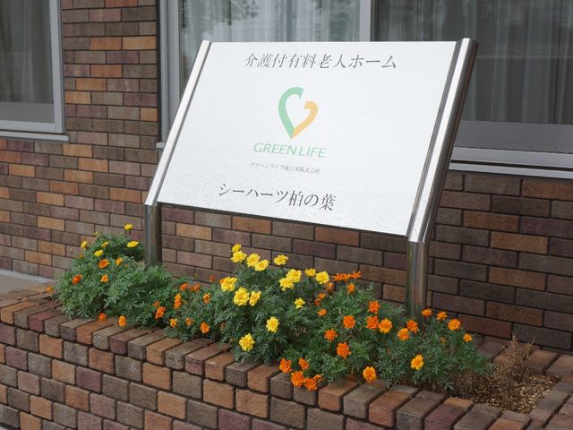 看板と花壇の様子 エントランス前 シンボルカラーの緑が心地よい、"GREENLIFE"の看板がお出迎えします。明るく清潔な印象を与える入口で、私たちの施設の概要をひと目で感じていただけます。