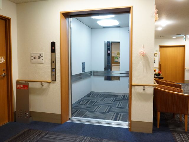 清潔なエレベーターホール エレベーター 広々とした待合スペースには、落ち着いた色合いのベンチが配置され、ゆったりとした時間をお過ごしいただけます。車椅子ユーザーも利用しやすい、広々としたエレベーターが整備されています。
