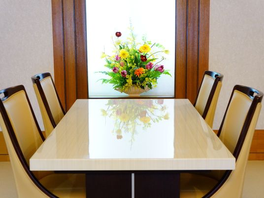 談話室は、4人用のテーブルと椅子が置かれている。真新しいテーブルには、壁際の花の置物が反映されている。