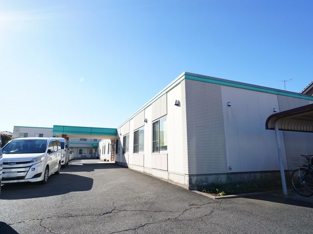 快晴の下の一階建て建物 外観 日差しに包まれた温かな雰囲気の建物前面です。このような環境で、あなたも一緒に働きませんか？