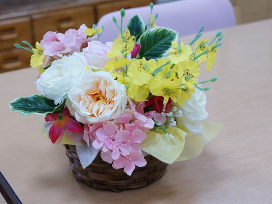 利用者が集うリビングルームの机の上には、ピンクや黄色など色鮮やかな造花の入った木製のかごが置かれている。