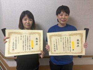表彰状を持つ女性2人の室内  